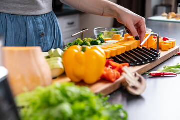 Woman lays sliced ​​vegetables on grill grate, in the home kitchen. Blured foreground.
