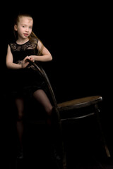 Portrait of a girl standing on a black background near the old Viennese chair.