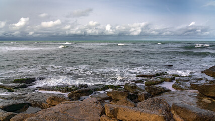 Empty rocky beach and stormy sea in cloudy weather