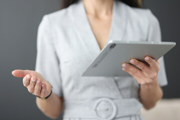 Business woman holding tablet in hands and waving her hand in office