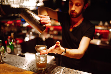 Expert barman is making  refreshing cocktail at night club. Bartender pouring strong and fresh  drink into the cocktail glass on the bar counter. Party, celebration, holidays.