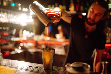Expert barman is making  refreshing cocktail at night club. Bartender pouring strong and fresh  drink into the cocktail glass on the bar counter. Party, celebration, holidays.