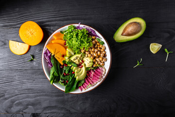 Buddha bowl, healthy and balanced food. roasted chickpeas, avocado, persimmon, spinach, avocado, watermelon radish and seeds. top view