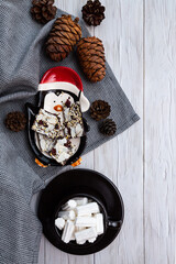 Cozy, winter, minimalistic still life with cedar cones, chocolate and a cup of marshmallows on a light wooden table top view