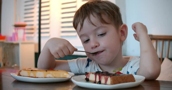 Cute healthy preschooler eating sweet cheesecake sitting in a children's cafe. At the restaurant Happy child eats a healthy organic cake with raspberry jam. Childhood, health and baby food concept.