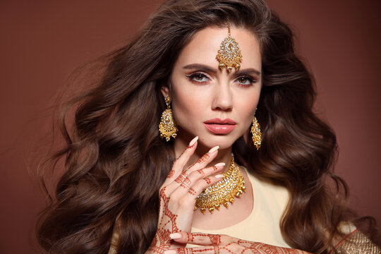 Wavy hair. Portrait of beautiful woman with indian jewelry. Young brunette model with Traditional Indian golden bijouterie set. Mehendi Henna painting on hand.