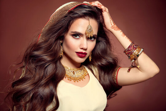 Wavy hair. Portrait of beautiful girl with indian jewelry. Young woman model with kundan golden bijouterie set. Traditional Indian costume lehenga. Mehendi Henna painting on hand.