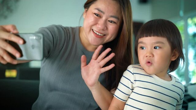 Family and technology concept, Asian happy Mother and daughter having fun while using App on smartphone and taking or video call with Father. 
