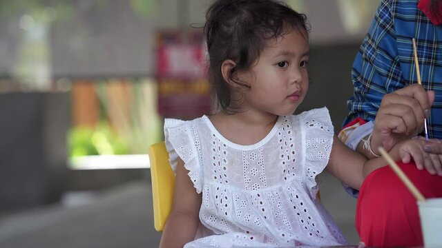 Cute little girl is painting on her hand with brush.