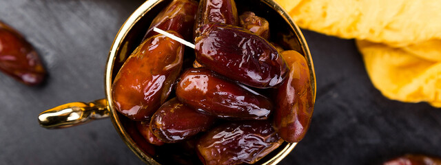 Banner of Dry fruit dates in golden cup near slate black heart. Copy space.