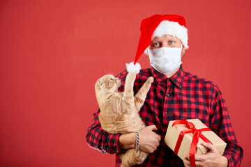 Man in protective face mask and Santa hat with Christmas DIY gift and a cat.