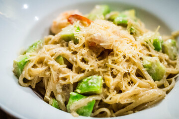 spaghetti with avocado, shrimp, seafood and parmesan on top served in a white bowl