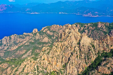 Aerial view of beautiful view of sunlit red mountains and the Mediterranean Sea with the Bay of Porto in Calanches area on Corsica island