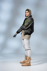 full length of young trendy man in hat, hoodie and anorak posing on grey © LIGHTFIELD STUDIOS