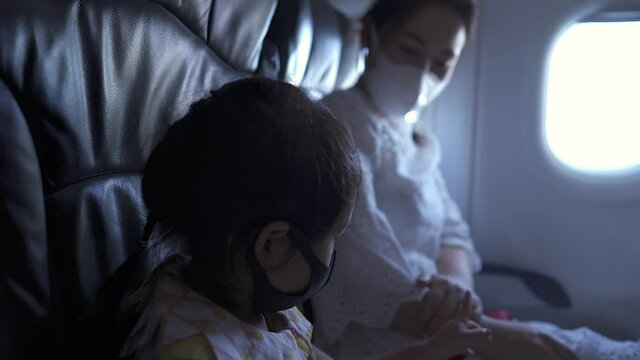 Mother and daughter sitting in airplane wearing protective face mask to prevent virus.