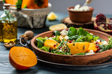 Healthy salad with persimmons, spinach, nuts, goat cheese, pomegranate and pumpkin seeds. Fitness food. Superfoods Vitamin autumn persimmon salad. Healthy food