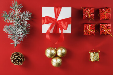 White box with a gift and a red bow, around Christmas decorations with fir branches on a red background