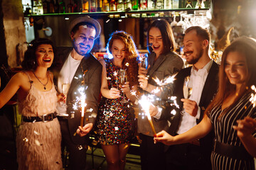 Friends celebrate Christmas or New Years party with sparklers and champagne. Group of happy people...