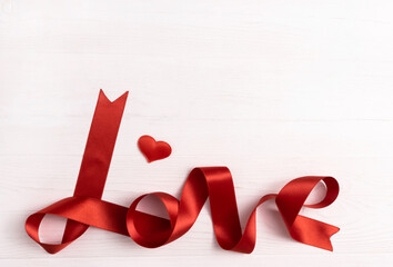 The word Love is written with red ribbon on a white wooden background with space for text. Postcard template for the holiday. Poster.