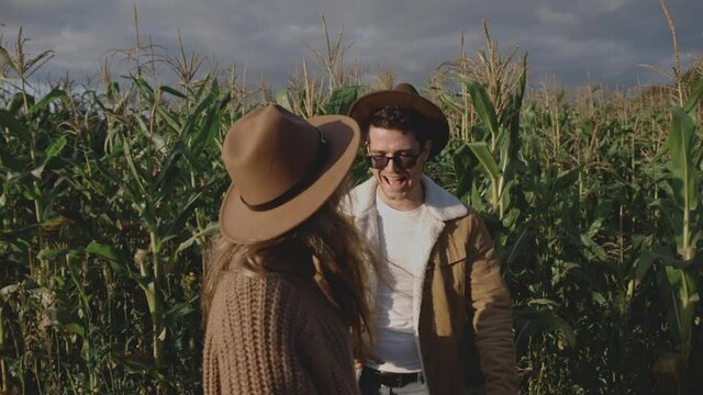 Close up of hipster girl in brown hat leading young millennial man through field with crops. Guys spending time together on date outside city. Little trip or travel in countryside. Family concept.