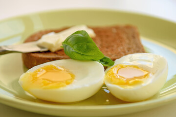 Two soft-boiled egg halves on a plate. Basil leaf, toast and butter. Close up.