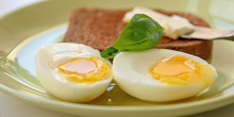 Two soft-boiled egg halves on a plate. Basil leaf, toast and butter. Close up.