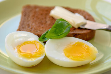 Two soft-boiled egg halves on a plate. Basil leaf, toast and butter. Close up.