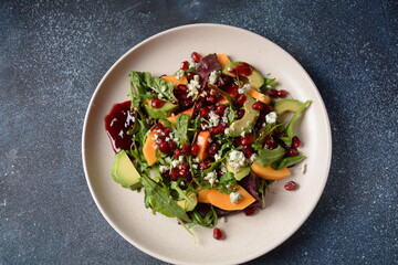 Healthy salad persimmon, blue cheese, spinach, arugula, lettuce leaves on white plate