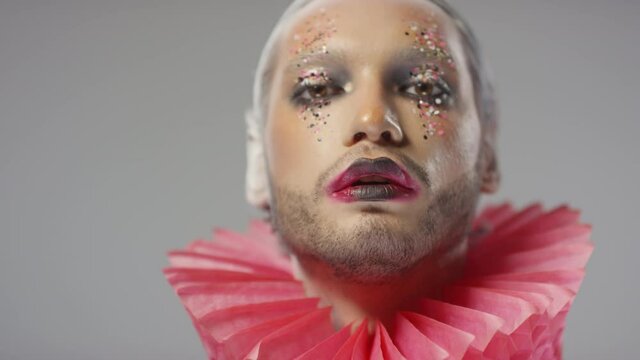 Close up portrait shot of handsome man with theatrical make-up and red ruff around his neck miming for camera