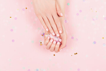 Obraz na płótnie Canvas Manicure and nail care concept. Woman hands are holding pastel confetti. Perfect pastel pink nail polish. Party, holidays or celebration vibes.