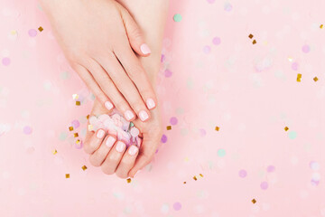 Manicure and nail care concept. Woman hands are holding pastel confetti. Perfect pastel pink nail polish. Party, holidays or celebration vibes.