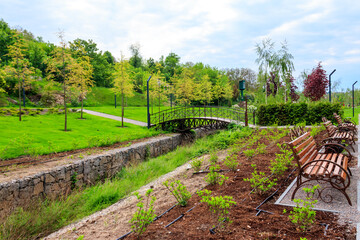 Beautiful view of the city park with arched footbridge across small river and young trees