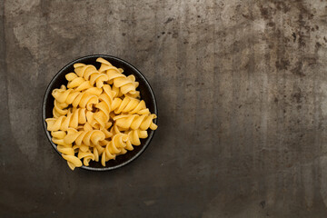 Fusilli pasta dentro de un cuenco negro sobre un fondo oscuro. Vista superior. Copy space