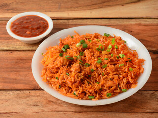 Tasty schezwan chicken fried rice with tomato sauce served in white bowl over a rustic wooden background, Indian cuisine, selective focus