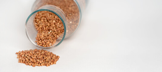 Buckwheat falls from a glass container on a white table