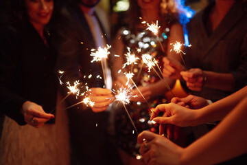 Glowing sparkles in hands. Group of happy people enjoying party with fireworks. Winter holiday,...