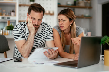 Worried couple paying their bills online with laptop at home in the living room. Couple having financial problems..