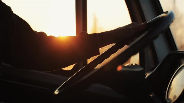 Close-up of a young man's hand on the steering wheel of a car on the background of sunset outside the window cabin