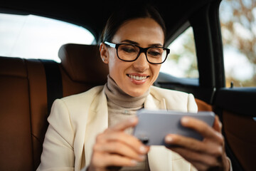 Beautiful smiling businesswoman using mobile phone while sitting in car