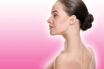 Fototapeta premium Young woman with perfect healthy skin and hair in bun on a pink background with a shaded white outline