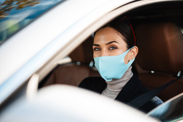 Beautiful confident pleased businesswoman in face mask driving car