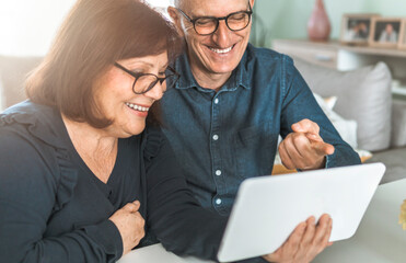 Middle aged couple smiling while shopping online - seniors chat with friends and family - warm filter on background.