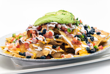 Avocado topped nachos with black beans, guacamole, sour cream, and pico de gallo stacked high on the plate.