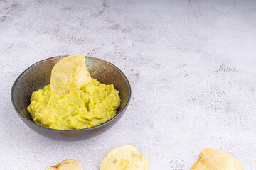 Guacamole on a bowl with potato chips on gray stone background. Organic avocado. Top view. Space for text. Concept of healthy fruit