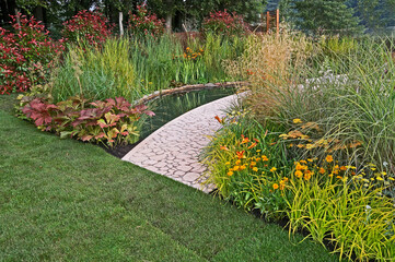 A garden with a water feature and selection of grasses, plants  and flowers