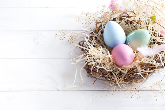 colorful easter eggs in small nest with on white wooden background, copy space. Holiday event