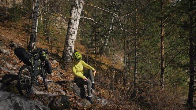 The woman travel on mixed terrain cycle touring with bikepacking. The traveler journey with bicycle bags. Sportswear in green black colors. The trip in magical autumn forest, river stream.