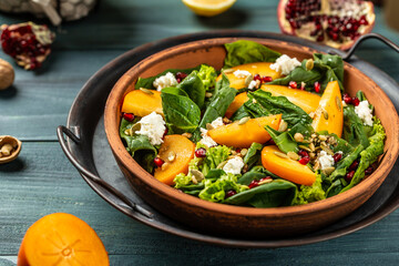 healthy delicious winter salad with persimmon slices, mix of spinach, nuts, goat cheese, pomegranate, pumpkin seeds. Healthy balanced eating. Top view