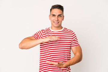 Obraz premium Young caucasian handsome man isolated holding something with both hands, product presentation.