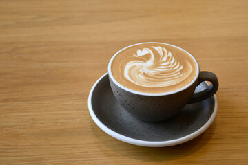 A hot latte cup with latte art on top put on wooden table.